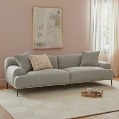 a living room with pink walls and white carpeted flooring, a gray sofa has two pillows on it