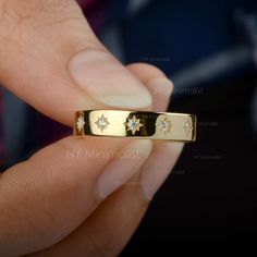 a person holding a gold ring with diamonds in their fingers and the middle one has a star design on it