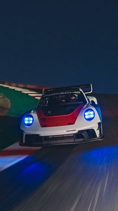 a red and white sports car driving down the road at night with its lights on