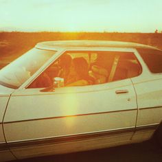 a white car with the sun setting behind it and people sitting in the driver's seat