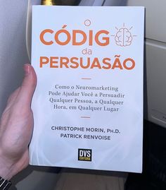 a person holding up a book in front of their face and hand, with the title code da persuasao written on it