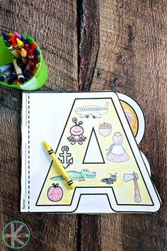 the letter a coloring book with crayons and pencils next to it on a wooden table