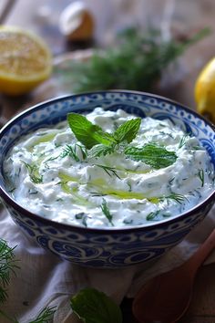 a blue and white bowl filled with yogurt surrounded by lemons, dill and parsley