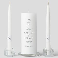 two white candles sitting next to each other on top of a glass stand with the words madison and kieran printed on it