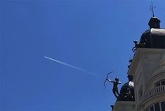 an airplane flying in the sky over a building with statues on it's roof