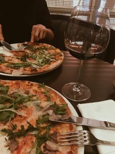 two pizzas sitting on top of white plates with forks and knives next to each other