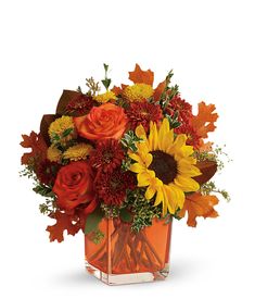 an orange vase filled with sunflowers and autumn leaves