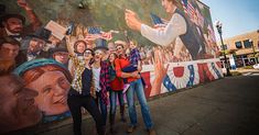 three women standing in front of a mural on the side of a building with people holding american flags