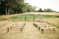 an outdoor ceremony set up with wooden benches and greenery on the ground, surrounded by tall grass