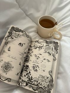 an open book sitting on top of a white bed next to a cup of coffee