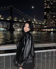 a woman standing on the side of a bridge next to a body of water at night