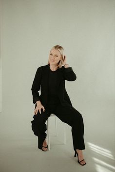 a woman sitting on top of a white chair next to a window with her hand in her hair