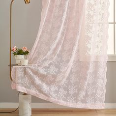 a pink curtain with white lace on it next to a potted plant in front of a window