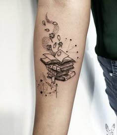 a person with a tattoo on their arm holding a book and flying birds in the sky