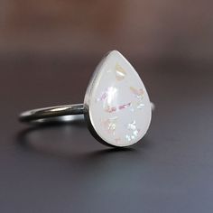 "Breastmilk jewelry teardrop 14x10mm stone sterling silver ring. Opal effect flakes can be added. To see our full breastmilk Ring collection, please click here: https://www.etsy.com/ca/shop/KeepsakeMom?ref=simple-shop-header-name&listing_id=1095328032&section_id=24695275 To see All our items, please click here: https://www.etsy.com/ca/shop/KeepsakeMom?ref=simple-shop-header-name&listing_id=1095328032 BREASTMILK JEWELRY NOTICE: For jewelry made with your own breast milk, please visit www.Keepsake Adjustable White Minimalist Opal Ring, White Minimalist Adjustable Opal Ring, White Adjustable Minimalist Opal Ring, White Teardrop Sterling Silver Rings, White Opal Jewelry Gift, Handmade White Opal Ring In Sterling Silver, White Moonstone Cabochon Promise Ring, Adjustable White Opal Ring In Sterling Silver, White Hypoallergenic Opal Jewelry