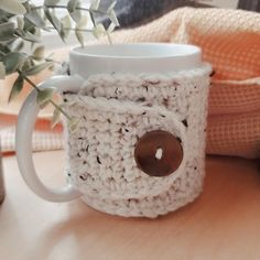 a crocheted coffee cup with a button on the side and a mug in front