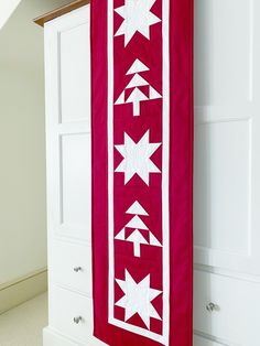 a red and white quilt hanging from the side of a wall next to a dresser