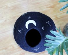 a black cat bed with stars and moon design on the top, next to a potted plant