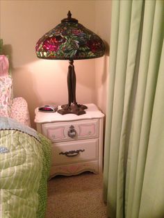 a lamp on top of a dresser next to a bed with green sheets and pillows