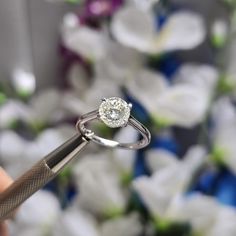 a person holding a diamond ring in front of white flowers with a large knife to cut it