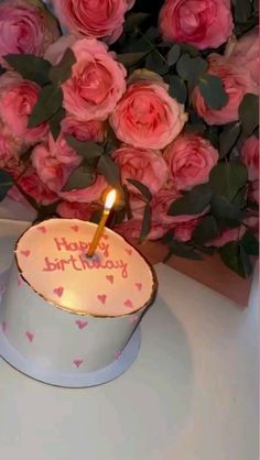 a birthday cake sitting on top of a table with pink roses in front of it