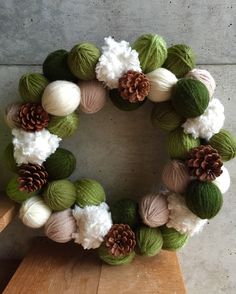 a yarn wreath with pine cones and balls of yarn on it sitting on a wooden table