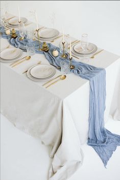 the table is set with white plates and silverware, blue napkins and gold place settings