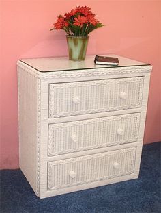 a white wicker dresser with red flowers on top and a pink wall behind it