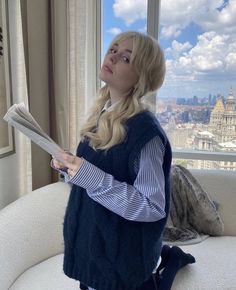 a woman sitting on top of a couch next to a window holding a paper in her hand