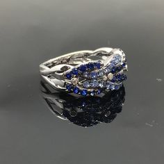 14K Sapphire and Diamond Band METAL: 14K White Gold TOTAL WEIGHT: DIAMONDS: 4 Round Brilliant Diamonds COLOR: G/H CLARITY: VS2 TOTAL WEIGHT: 0.04 ct GEMSTONES: Round brilliant cut blue sapphires TOTAL WEIGHT: 1.22 ct SIZE: Ladies size 5-8. Please indicate your ring size at checkout. DESCRIPTION: This gorgeous ring has a braided design of light and dark blue sapphires. It has four small bezel set diamonds in between each braid. It is 8.5mm wide with a 3mm height. The shank tapers down to 3mm. FRE Silver Cluster Sapphire Ring With Diamond Accents, Fine Jewelry Multi-stone Diamond Promise Ring, Cluster Sapphire Ring With Diamond Accents For Promise, 14k White Gold Sapphire Ring Fine Jewelry, Sapphire Cluster Rings With Diamond Accents, Fine Jewelry Multi-stone Promise Ring, Multi-stone Sapphire Rings For Anniversary, Sapphire Rings With Diamond Accents In Cluster Shape, Fine Jewelry Hallmarked Sapphire Open Ring