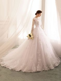 a woman in a white wedding dress standing next to a window with sheer drapes