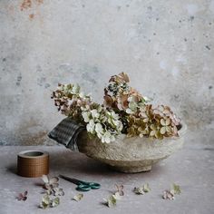 flowers in a stone bowl with scissors and thread on the ground next to it,