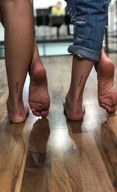 two people standing on top of a wooden floor with their bare feet in the air