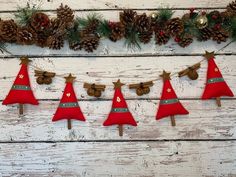 christmas decorations are hanging on a white wooden wall with pine cones and red felt trees