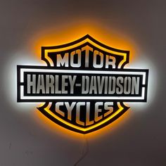 the harley davidson neon sign is lit up in front of a white wall with black lettering on it