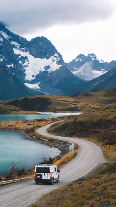 a van driving down a road next to a body of water with mountains in the background