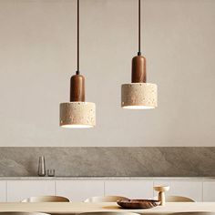 three pendant lights hanging over a table in a room with white walls and wooden chairs