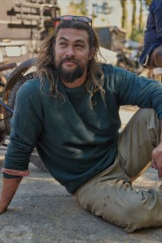 a man with long hair sitting on the ground