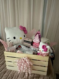 a hello kitty stuffed animal sits in a wooden crate on a bed with pink bows