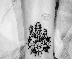 a black and white photo of a cactus tattoo on the wrist with flowers in it