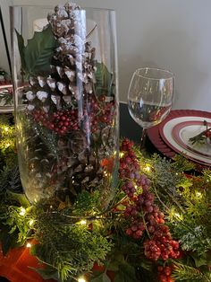 a glass vase filled with pine cones and greenery on top of a christmas table