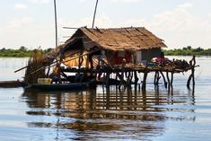 a house on stilts in the water with people standing around it and one boat