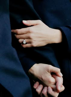 two hands holding each other while they are dressed in black and white attire with an engagement ring on their finger