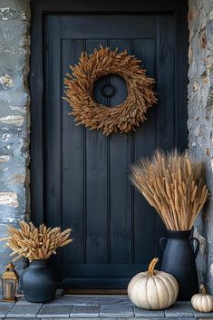 two black vases filled with dry grass next to a wreath and pumpkins on the doorstep