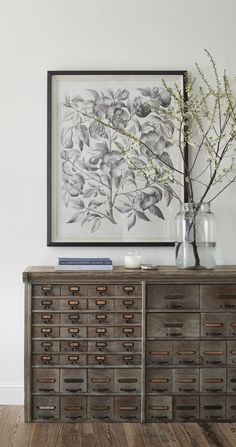 a vase with flowers on top of a wooden dresser next to a framed art piece