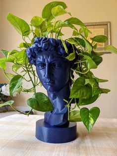 a blue busturine with green leaves in it's head on a table