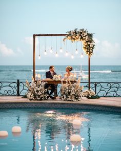 a bride and groom sitting at a table by the pool in front of an ocean