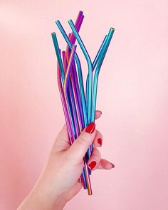 a hand holding up several colorful straws against a pink background