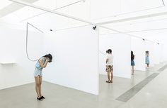 several people standing in an empty room with white walls and one person on the phone