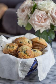 blueberry muffins in a basket on a table next to flowers and a vase